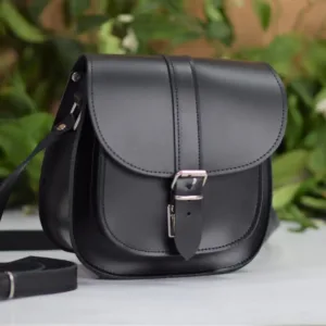 Μαύρη δερμάτινη τσάντα χιαστί πάνω σε επίπεδη επιφάνεια με φόντο φύλλα δέντρου.